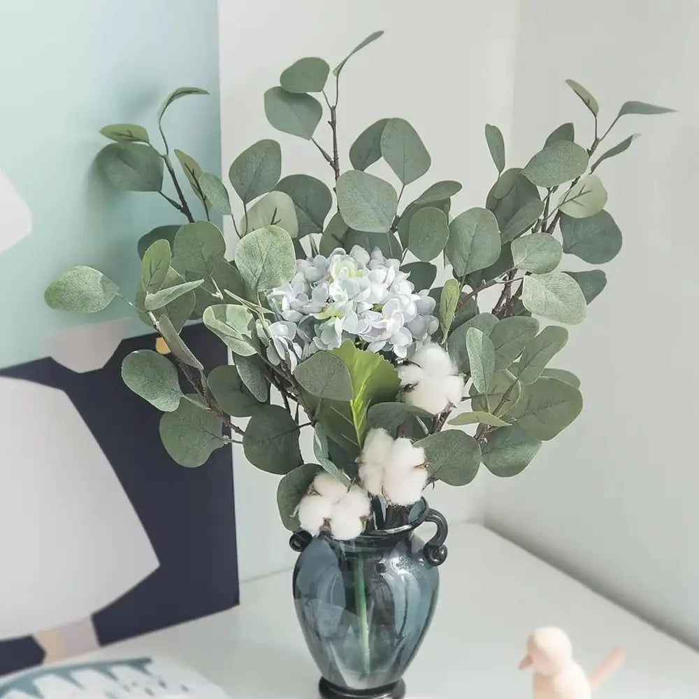 Vase en verre bleu foncé avec anses noires tenant bouquet d’eucalyptus artificiel, hortensias blancs et cotons moelleux