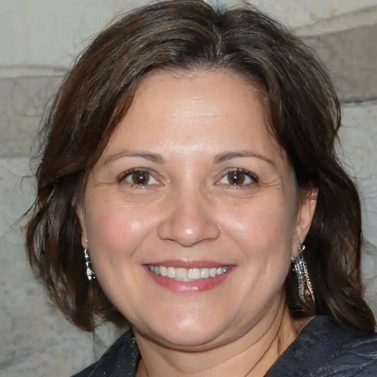 Une femme aux cheveux bruns mi-longs et au sourire chaleureux, portant des boucles d'oreilles argentées pendantes.