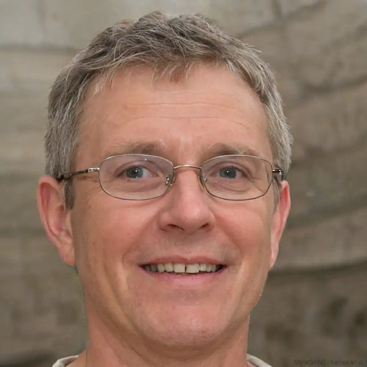 Un homme aux cheveux courts gris et aux yeux bleus portant des lunettes à monture fine.