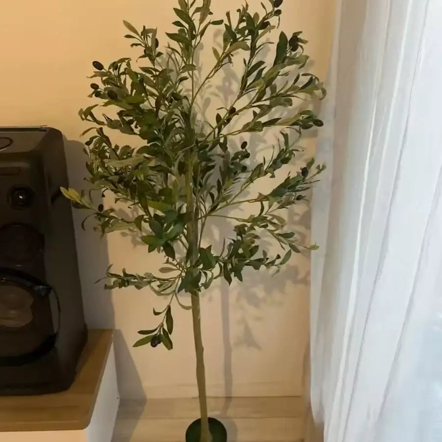 Un grand olivier artificiel aux feuilles vertes luxuriantes et aux olives pourpres foncées, debout dans un pot noir simple.